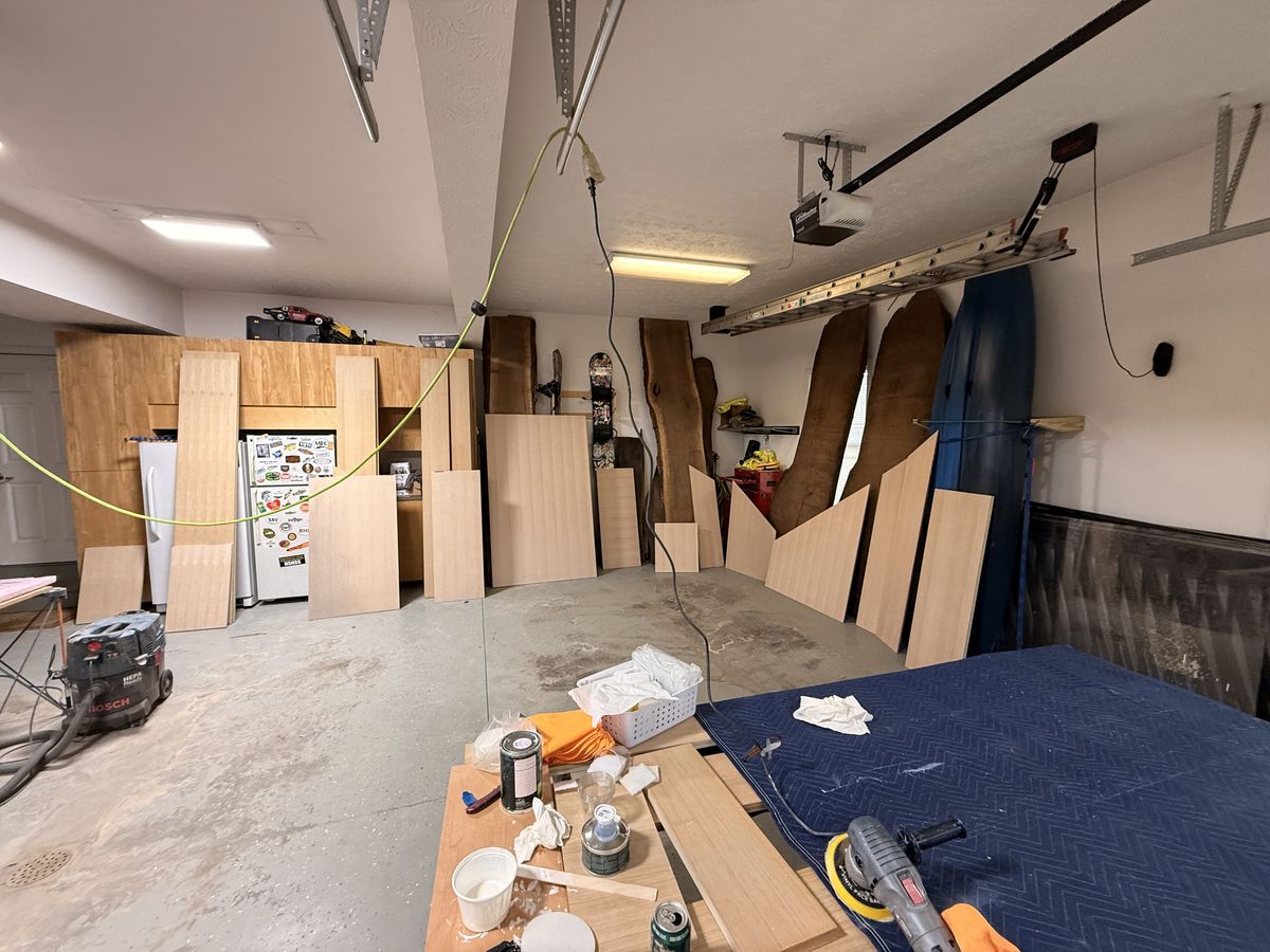 Garage wide shot with cut white oak closet panels standing upright, live edge slabs on the wall, and Rubio with other finishing supplies on the temporary workbench
