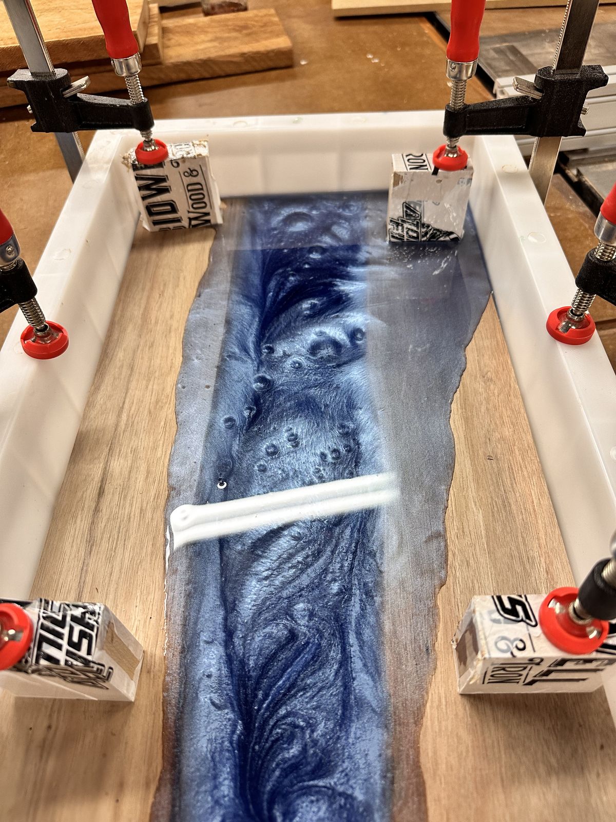 Blue epoxy resin being poured into a river board mold in the wood shop